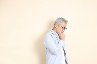 Doğu Asyalı bir adamın portresi gri saçlı ve gözlüklü, şık günlük kıyafetler giymiş, kahverengi arka planda duruyor..