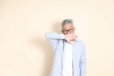 Doğu Asyalı bir adamın portresi gri saçlı ve gözlüklü, şık günlük kıyafetler giymiş, kahverengi arka planda duruyor..