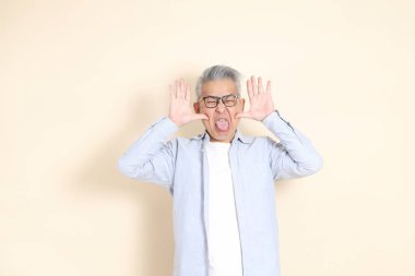 Doğu Asyalı bir adamın portresi gri saçlı ve gözlüklü, şık günlük kıyafetler giymiş, kahverengi arka planda duruyor..