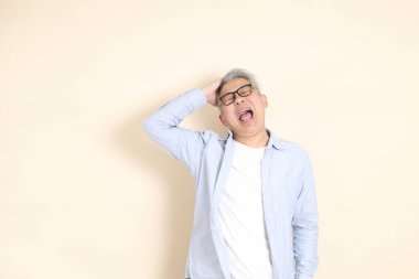 Doğu Asyalı bir adamın portresi gri saçlı ve gözlüklü, şık günlük kıyafetler giymiş, kahverengi arka planda duruyor..