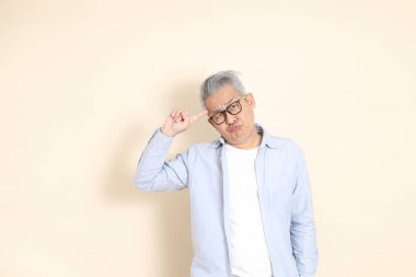 Doğu Asyalı bir adamın portresi gri saçlı ve gözlüklü, şık günlük kıyafetler giymiş, kahverengi arka planda duruyor..