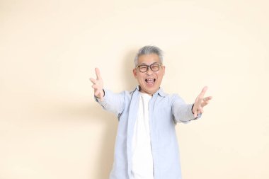 Doğu Asyalı bir adamın portresi gri saçlı ve gözlüklü, şık günlük kıyafetler giymiş, kahverengi arka planda duruyor..