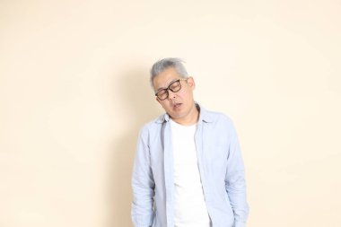 Doğu Asyalı bir adamın portresi gri saçlı ve gözlüklü, şık günlük kıyafetler giymiş, kahverengi arka planda duruyor..