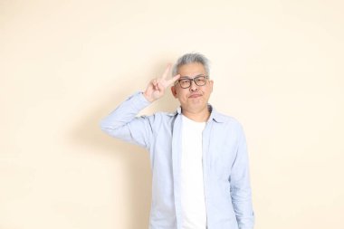 Doğu Asyalı bir adamın portresi gri saçlı ve gözlüklü, şık günlük kıyafetler giymiş, kahverengi arka planda duruyor..