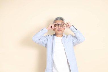 Doğu Asyalı bir adamın portresi gri saçlı ve gözlüklü, şık günlük kıyafetler giymiş, kahverengi arka planda duruyor..