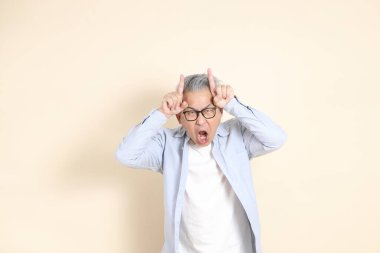 Doğu Asyalı bir adamın portresi gri saçlı ve gözlüklü, şık günlük kıyafetler giymiş, kahverengi arka planda duruyor..