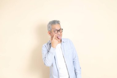 Doğu Asyalı bir adamın portresi gri saçlı ve gözlüklü, şık günlük kıyafetler giymiş, kahverengi arka planda duruyor..