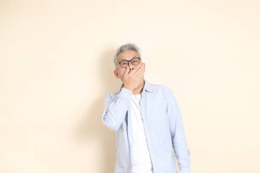 Doğu Asyalı bir adamın portresi gri saçlı ve gözlüklü, şık günlük kıyafetler giymiş, kahverengi arka planda duruyor..