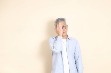 Doğu Asyalı bir adamın portresi gri saçlı ve gözlüklü, şık günlük kıyafetler giymiş, kahverengi arka planda duruyor..