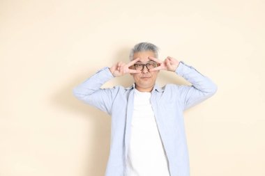 Doğu Asyalı bir adamın portresi gri saçlı ve gözlüklü, şık günlük kıyafetler giymiş, kahverengi arka planda duruyor..