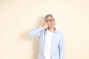 Doğu Asyalı bir adamın portresi gri saçlı ve gözlüklü, şık günlük kıyafetler giymiş, kahverengi arka planda duruyor..