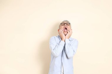 Doğu Asyalı bir adamın portresi gri saçlı ve gözlüklü, şık günlük kıyafetler giymiş, kahverengi arka planda duruyor..