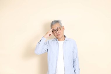 Doğu Asyalı bir adamın portresi gri saçlı ve gözlüklü, şık günlük kıyafetler giymiş, kahverengi arka planda duruyor..