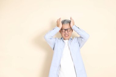 Doğu Asyalı bir adamın portresi gri saçlı ve gözlüklü, şık günlük kıyafetler giymiş, kahverengi arka planda duruyor..