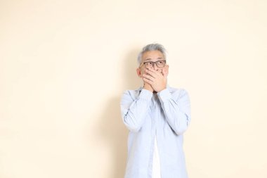 Doğu Asyalı bir adamın portresi gri saçlı ve gözlüklü, şık günlük kıyafetler giymiş, kahverengi arka planda duruyor..