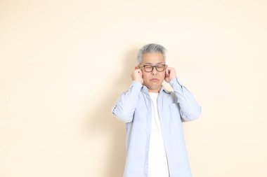 Doğu Asyalı bir adamın portresi gri saçlı ve gözlüklü, şık günlük kıyafetler giymiş, kahverengi arka planda duruyor..