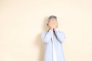 Doğu Asyalı bir adamın portresi gri saçlı ve gözlüklü, şık günlük kıyafetler giymiş, kahverengi arka planda duruyor..