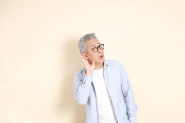 Doğu Asyalı bir adamın portresi gri saçlı ve gözlüklü, şık günlük kıyafetler giymiş, kahverengi arka planda duruyor..