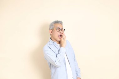 Doğu Asyalı bir adamın portresi gri saçlı ve gözlüklü, şık günlük kıyafetler giymiş, kahverengi arka planda duruyor..