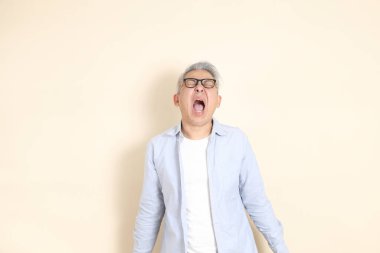 Doğu Asyalı bir adamın portresi gri saçlı ve gözlüklü, şık günlük kıyafetler giymiş, kahverengi arka planda duruyor..