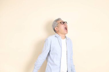 Doğu Asyalı bir adamın portresi gri saçlı ve gözlüklü, şık günlük kıyafetler giymiş, kahverengi arka planda duruyor..