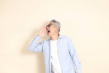 Doğu Asyalı bir adamın portresi gri saçlı ve gözlüklü, şık günlük kıyafetler giymiş, kahverengi arka planda duruyor..