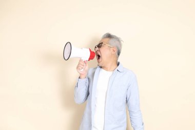 Doğu Asyalı bir adamın portresi gri saçlı ve gözlüklü, şık günlük kıyafetler giymiş, kahverengi arka planda duruyor..