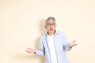 Doğu Asyalı bir adamın portresi gri saçlı ve gözlüklü, şık günlük kıyafetler giymiş, kahverengi arka planda duruyor..