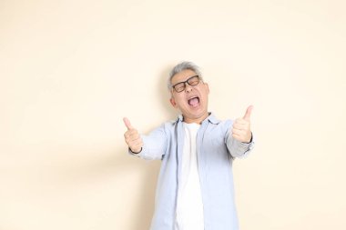 Doğu Asyalı bir adamın portresi gri saçlı ve gözlüklü, şık günlük kıyafetler giymiş, kahverengi arka planda duruyor..