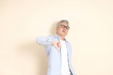 Doğu Asyalı bir adamın portresi gri saçlı ve gözlüklü, şık günlük kıyafetler giymiş, kahverengi arka planda duruyor..