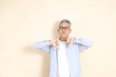 Doğu Asyalı bir adamın portresi gri saçlı ve gözlüklü, şık günlük kıyafetler giymiş, kahverengi arka planda duruyor..