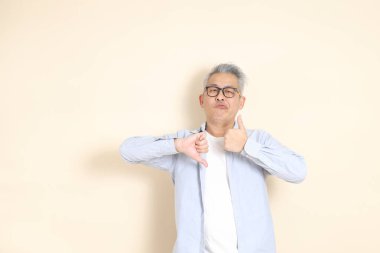 Doğu Asyalı bir adamın portresi gri saçlı ve gözlüklü, şık günlük kıyafetler giymiş, kahverengi arka planda duruyor..