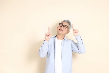 Doğu Asyalı bir adamın portresi gri saçlı ve gözlüklü, şık günlük kıyafetler giymiş, kahverengi arka planda duruyor..