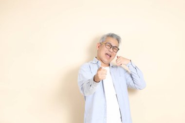 Doğu Asyalı bir adamın portresi gri saçlı ve gözlüklü, şık günlük kıyafetler giymiş, kahverengi arka planda duruyor..