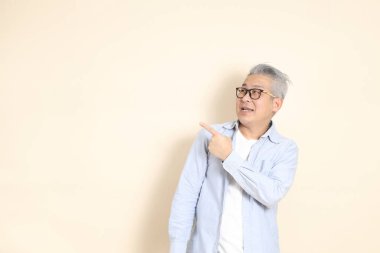 Doğu Asyalı bir adamın portresi gri saçlı ve gözlüklü, şık günlük kıyafetler giymiş, kahverengi arka planda duruyor..