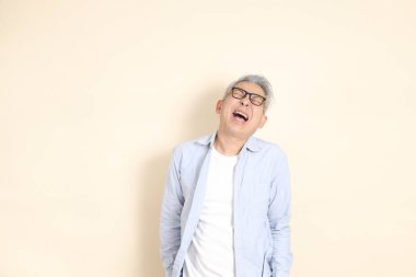 Doğu Asyalı bir adamın portresi gri saçlı ve gözlüklü, şık günlük kıyafetler giymiş, kahverengi arka planda duruyor..