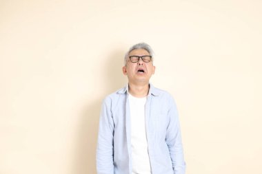 Doğu Asyalı bir adamın portresi gri saçlı ve gözlüklü, şık günlük kıyafetler giymiş, kahverengi arka planda duruyor..