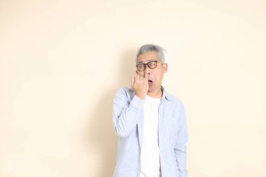 Doğu Asyalı bir adamın portresi gri saçlı ve gözlüklü, şık günlük kıyafetler giymiş, kahverengi arka planda duruyor..