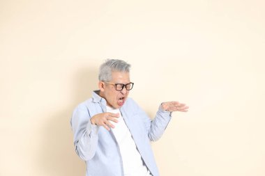 Doğu Asyalı bir adamın portresi gri saçlı ve gözlüklü, şık günlük kıyafetler giymiş, kahverengi arka planda duruyor..