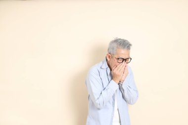 Doğu Asyalı bir adamın portresi gri saçlı ve gözlüklü, şık günlük kıyafetler giymiş, kahverengi arka planda duruyor..