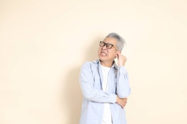 Doğu Asyalı bir adamın portresi gri saçlı ve gözlüklü, şık günlük kıyafetler giymiş, kahverengi arka planda duruyor..