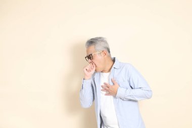 Doğu Asyalı bir adamın portresi gri saçlı ve gözlüklü, şık günlük kıyafetler giymiş, kahverengi arka planda duruyor..