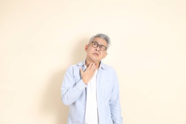 Doğu Asyalı bir adamın portresi gri saçlı ve gözlüklü, şık günlük kıyafetler giymiş, kahverengi arka planda duruyor..