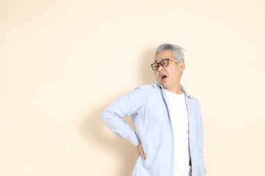 Doğu Asyalı bir adamın portresi gri saçlı ve gözlüklü, şık günlük kıyafetler giymiş, kahverengi arka planda duruyor..