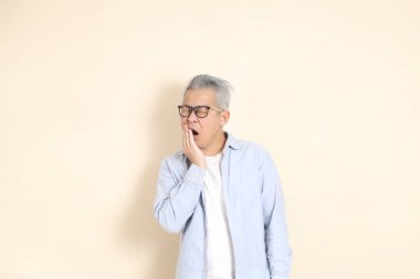 Doğu Asyalı bir adamın portresi gri saçlı ve gözlüklü, şık günlük kıyafetler giymiş, kahverengi arka planda duruyor..