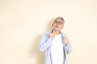 Doğu Asyalı bir adamın portresi gri saçlı ve gözlüklü, şık günlük kıyafetler giymiş, kahverengi arka planda duruyor..