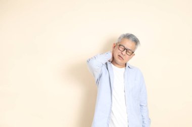 Doğu Asyalı bir adamın portresi gri saçlı ve gözlüklü, şık günlük kıyafetler giymiş, kahverengi arka planda duruyor..