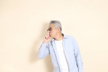 Doğu Asyalı bir adamın portresi gri saçlı ve gözlüklü, şık günlük kıyafetler giymiş, kahverengi arka planda duruyor..