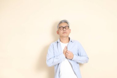 Doğu Asyalı bir adamın portresi gri saçlı ve gözlüklü, şık günlük kıyafetler giymiş, kahverengi arka planda duruyor..