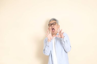 Doğu Asyalı bir adamın portresi gri saçlı ve gözlüklü, şık günlük kıyafetler giymiş, kahverengi arka planda duruyor..